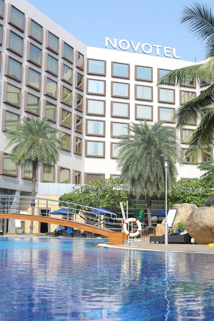 Contemporary hotel exterior with a pool, palm trees, and clear blue skies.