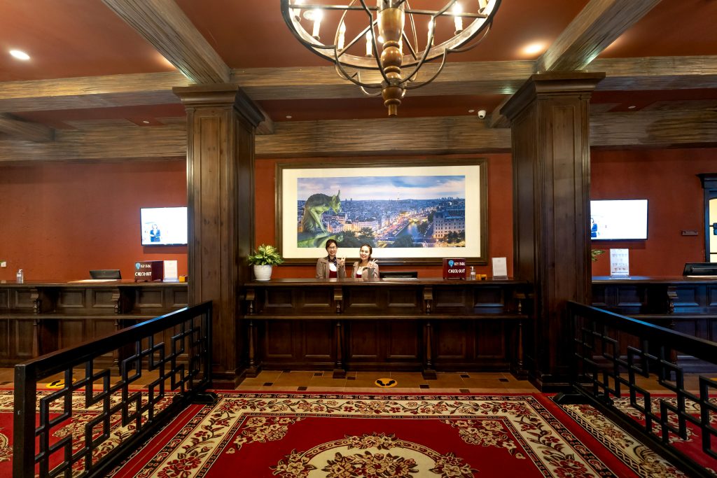 Luxurious hotel lobby featuring receptionists at front desk framed by vintage decor and chandelier.