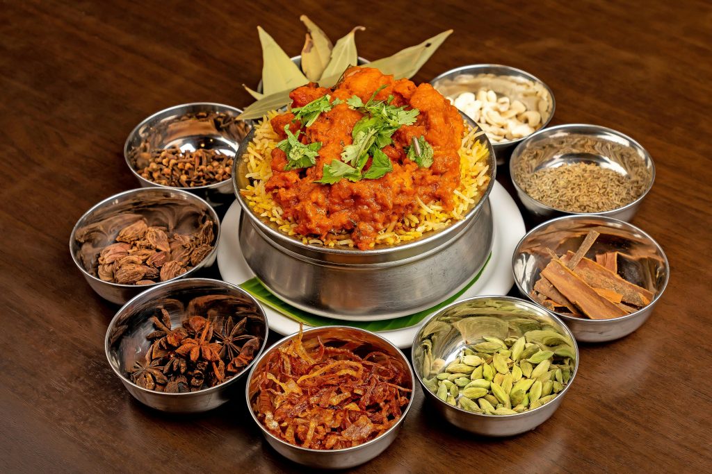 Delicious chicken biryani in a bowl with raw ingredients and spices around it